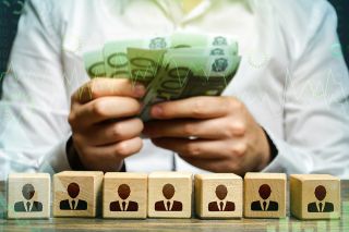 © Andrii Yalanskyi - Adobe Stock.com Foto: Figuren auf Würfeln und Hände mit Geldscheinen