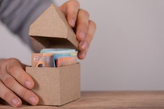 © vegefox.com - stock.adobe.com Foto: Schachtel in Hausform mit Geldscheinen